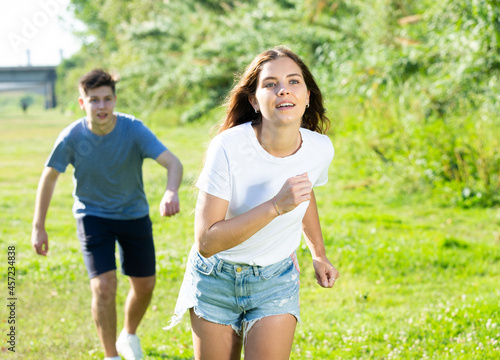 Two teenagers are running on the grass in summertime