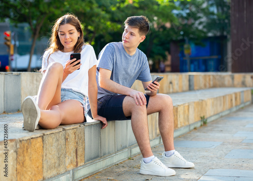 Young man and girl are sitting and watching in their smartphones