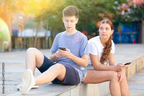 Two young people with mobile phones are sitting on the step