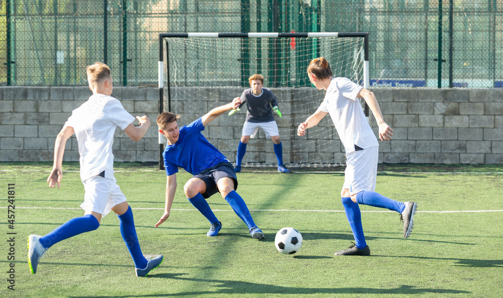 Fototapeta premium Game moments of football match between two teams of teenagers in white and blue shirts