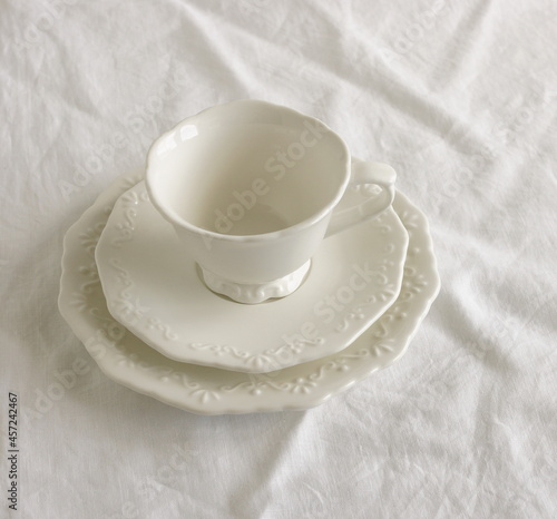 White ceramic coffee cup and sausers set top view on white linen tablecloth. Mockup classic porcelain utensils.Clean dishes for text . Business food brand template. photo