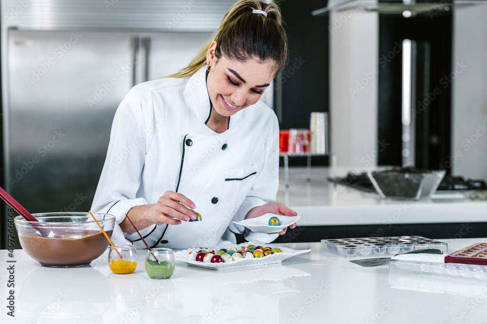 young hispanic woman chocolatier in chef hat with mexican chocolates candies on plate in a commercial kitchen in Mexico Latin America young hispanic woman chocolatier in chef hat with mexican chocolates candies on plate in a commercial kitchen in Mexico Latin America