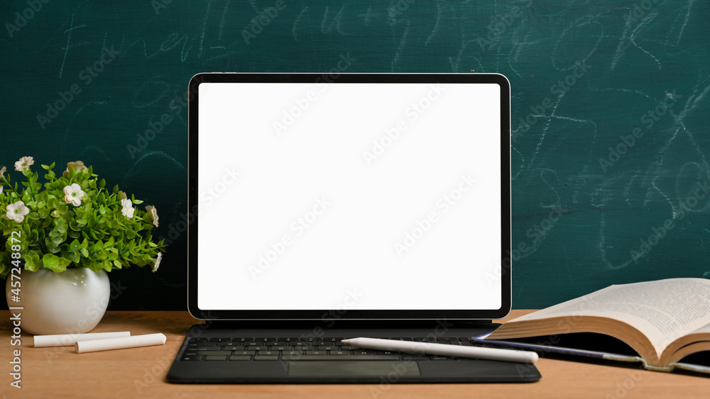 Back to school. Digital tablet with magic keyboard and stylus pen over green blackboard