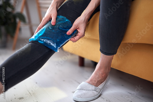 Woman with knee pain injury at home using ice gel pack.