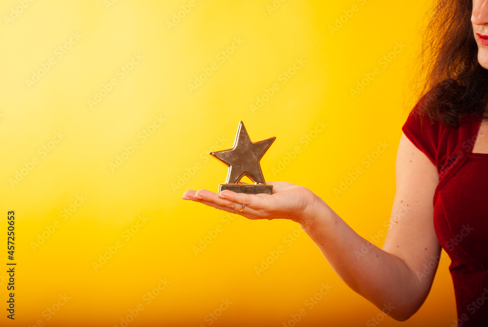 a woman holds a statuette in the form of a star in her hand on a boat in isolation on a yellow background. The concept of a movie star of victory or discounts a woman holds a statuette in the form of a star in her hand on a boat in isolation on a yellow background. The concept of a movie star of victory or discounts