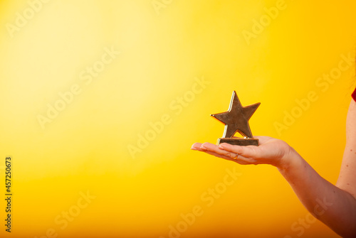 a woman holds a statuette in the form of a star in her hand on a boat in isolation on a yellow background. The concept of a movie star of victory or discounts