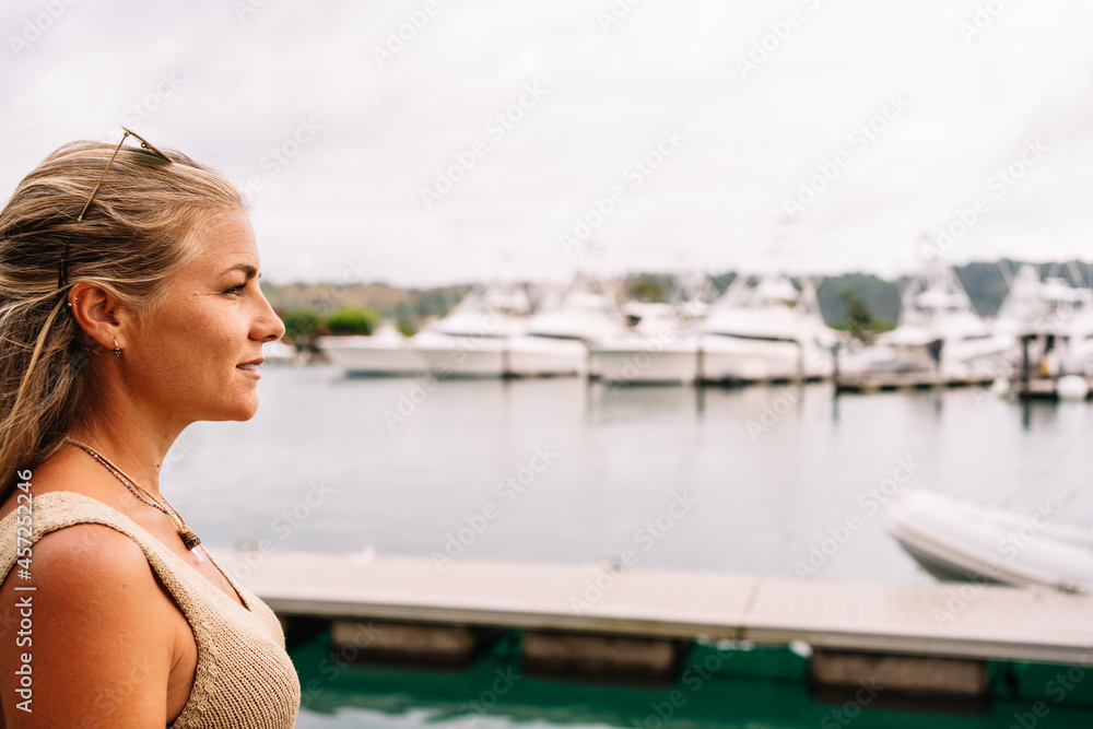 Blonde woman in a pier looking at moored yachts