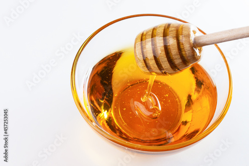 Sweet honey. Healthy organic honey dripping from wooden honey dipper in a bowl on white background. Sweet healthy dessert.