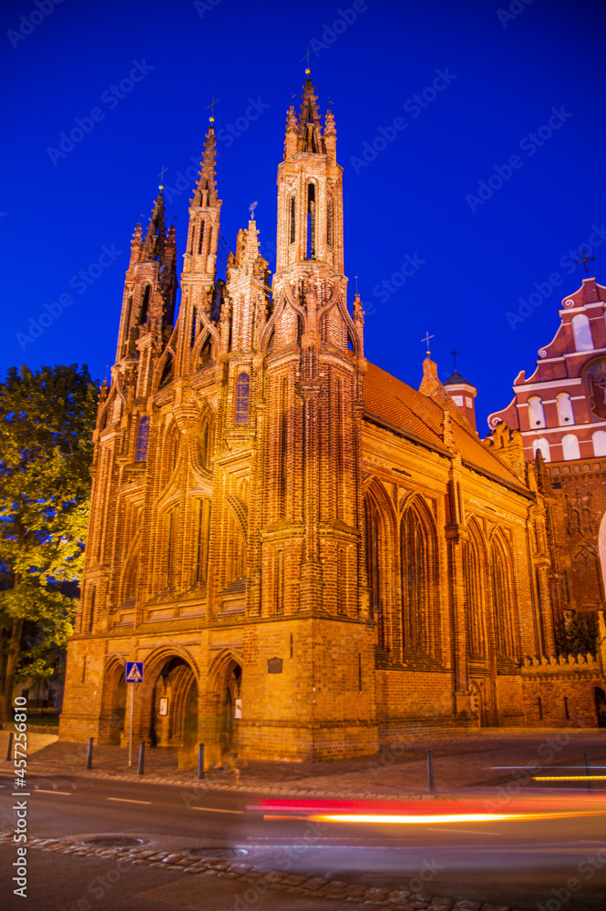 Illuminated beautiful old Orthodox Church in the old Town of Vilnius. Building with Gothic towers on The Main city street at night after sunset with the light trails. Car's motion blur
