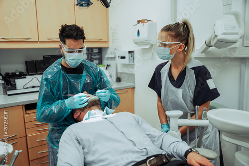 Caucasian male and female dentists standing in doctors room while operating on male clients teeth