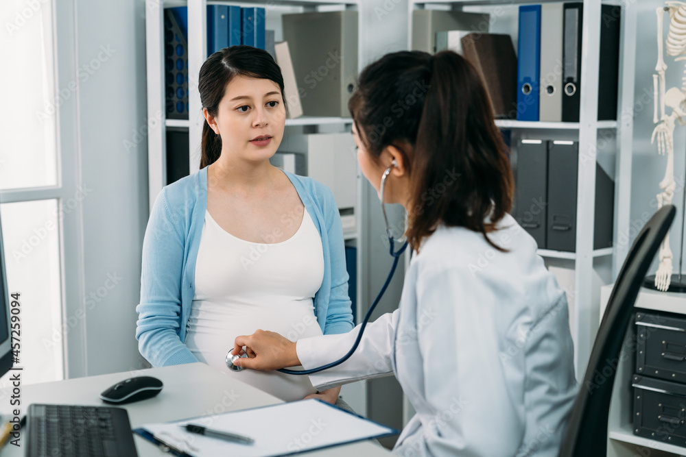 Fototapeta premium asian woman having pregnancy checkup while the gynecologist is using a stethoscope on her belly to listen to baby heartbeat in the clinic.