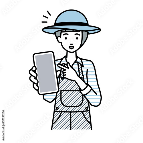 立ってスマートフォンを指差してこちらに向けて見せている農家の女性