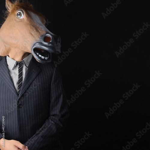 馬のマスク姿のビジネスマン／下手にでる・近づく・擦り寄る（黒背景）