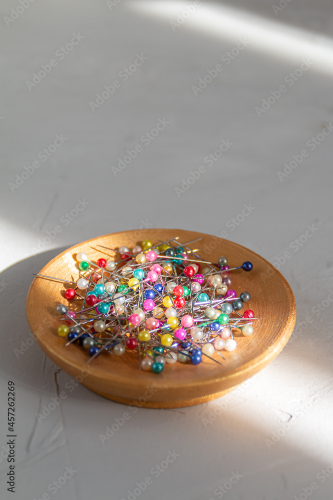 colored sewing pins in a golden plate against grey background with abstract light and shadow