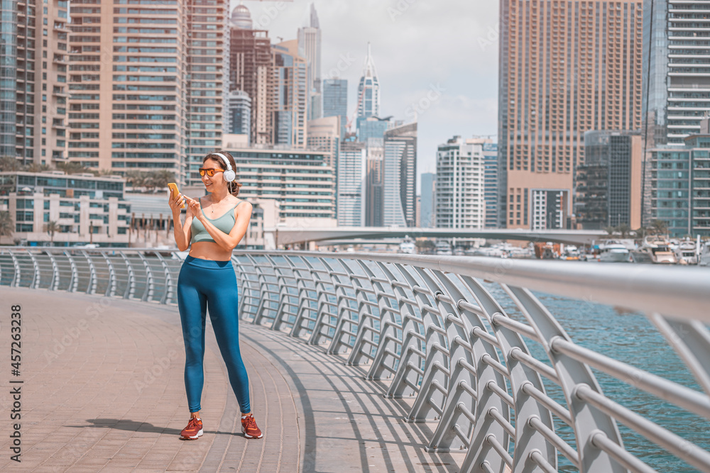 Woman was running along the Dubai Marina embankment and listens to music with headphones and using her smartphone Woman was running along the Dubai Marina embankment and listens to music with headphones and using her smartphone