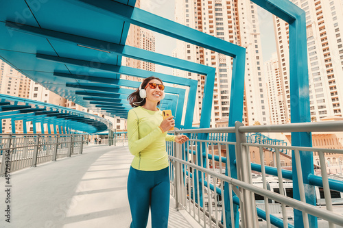Young woman in bright sportswear quickly runs across a pedestrian bridge in the Dubai Marina district. The concept of a female healthy lifestyle and fitness