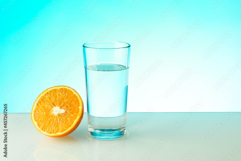 glass of water and half of orange on blue background with copy space. vitamin C concept. glass of water and half of orange on blue background with copy space. vitamin C concept.