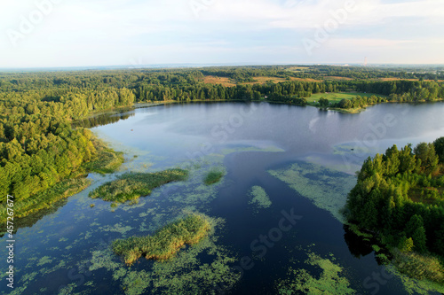 Lake among green trees in the countryside. Aerial view of a large lake or river against a blue sky. Ecology and wetlands concept
