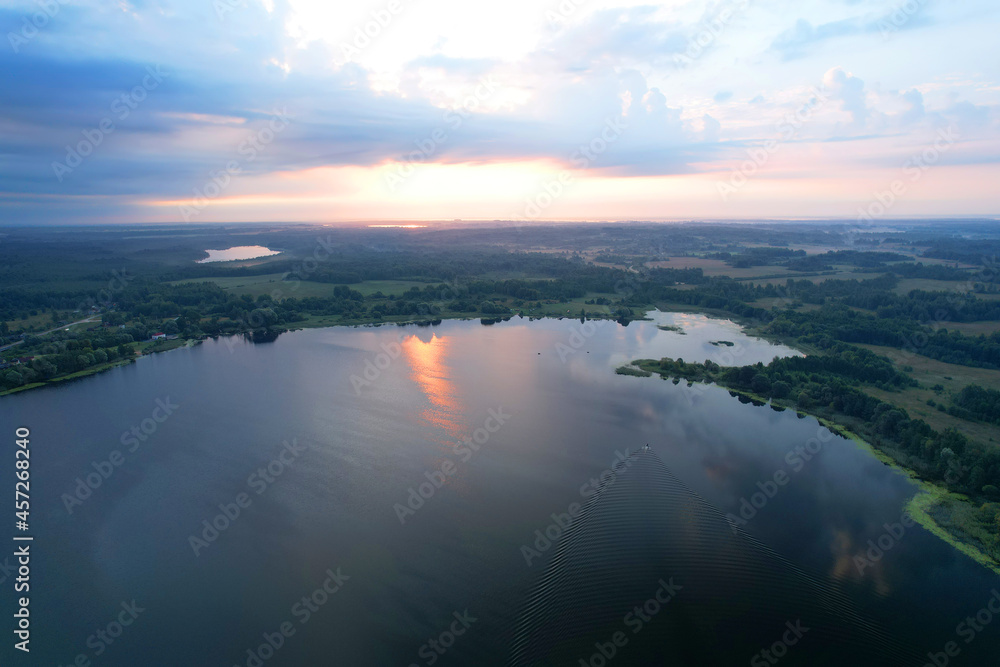Lake among green trees in the countryside. Aerial view of a large lake or river against the backdrop of a sunset. Ecology and wetlands concept.