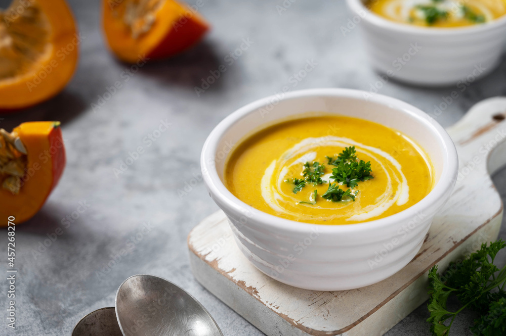 Pumpkin soup with coconut milk and squash slices. Creammy autumn soup in white bowl on gray background. Pumpkin soup with coconut milk and squash slices. Creammy autumn soup in white bowl on gray background.