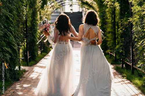 Foto Two happy lesbian LGBT brides wearing boho dresses walking through alley on thei