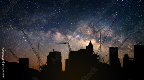 Silhouette of crane tower in the construction site city building with stary night sky and milky way background