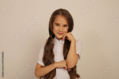 a beautiful teenage girl with long ponytails in a white shirt shows emotions on a white background