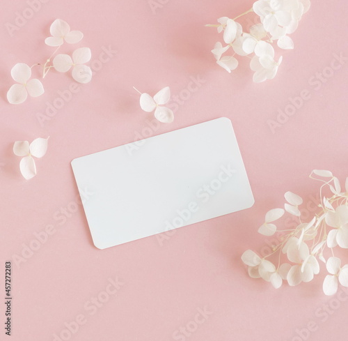 Blank paper with copy space and dry white flowers on pink background. top view. Card mockup,Greetings, wedding invitations blank, paper sheet.  Flowers template. © irenastar
