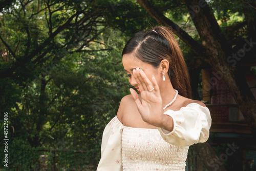 A young woman playfully pleads to not have her photo taken while at the park. Self conscious about her image.