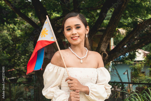 A classy and proud Filipina in an elegant off-shoulder dress and holding a Philippine flag.