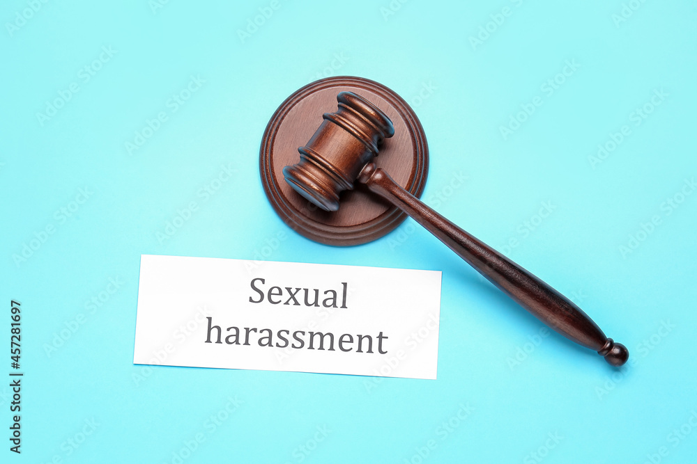 Paper with text SEXUAL HARASSMENT and judge's gavel on color background