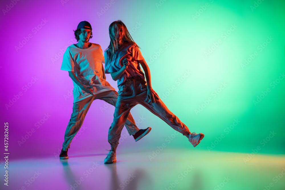 Stylish young hip-hop dancers, emotive girl and boy in action and motion in  casual sports youth clothes on gradient multi colored background at dance  hall in neon light. Stock Photo | Adobe