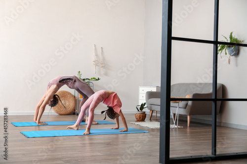 Quadro su tela Little girl with her mother practicing yoga at home