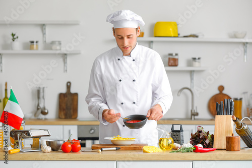 Italian chef pouring sauce into plate with pasta in kitchen
