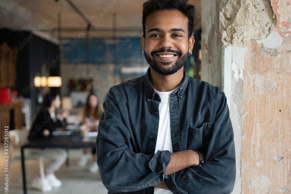 Fototapeta premium Portrait of mixed-race young man standing in office with colleagues meeting in background