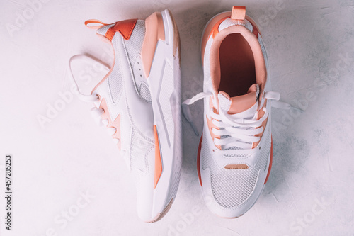 White women's sneakers with coral inserts on white concrete background. Top view, flat lay.
