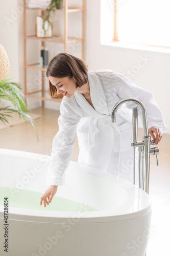 Young woman running bathtub with warm water at home