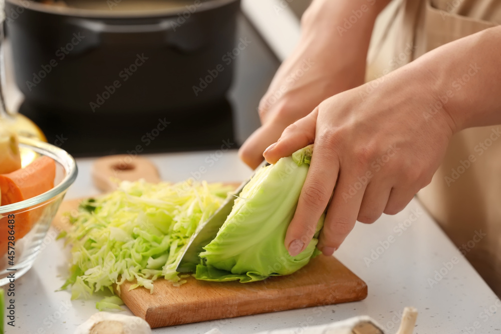 Young woman cutting cabbage for delicious borscht on wooden board in kitchen Young woman cutting cabbage for delicious borscht on wooden board in kitchen