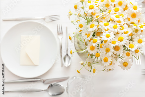 Stylish table setting and chamomile flowers on light background