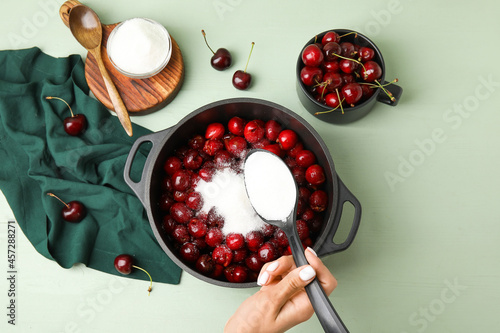 Bilde på lerret Woman preparing sweet cherry jam on color wooden background