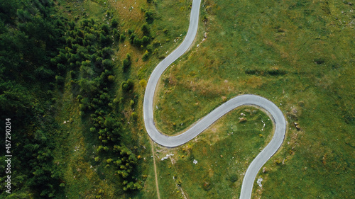 Aerial view of green fields  coniferous forest and narrow road in the Alps. Pathway in the mountains  directly above.