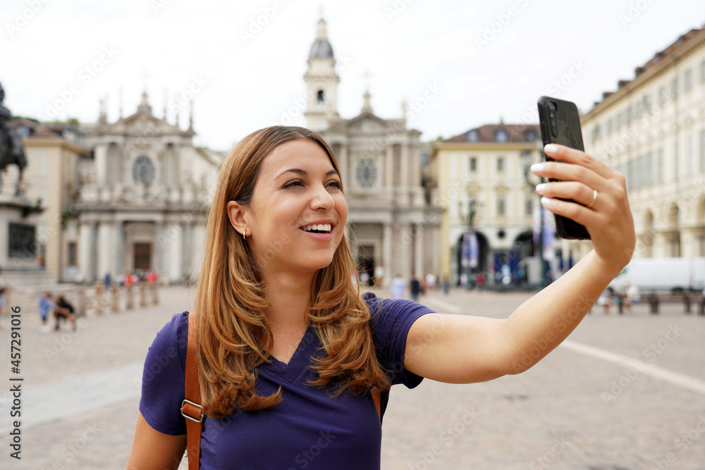 Tourist girl video calling and showing cityscape during her travel in Europe. Young traveler woman on landmark city square makes selfie or sharing her experience on vlog, Turin, Italy.