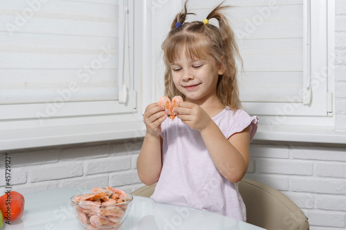 caucasian child girl eating shrimp at the table. healthy food concept. seafood in the diet of children
