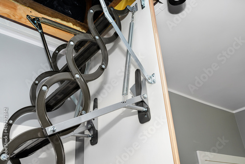 A spring tensioning mechanism that facilitates the opening of a metal ladder to the attic, as well as hinges and stabilizers, located in the ceiling of the house. © Michal