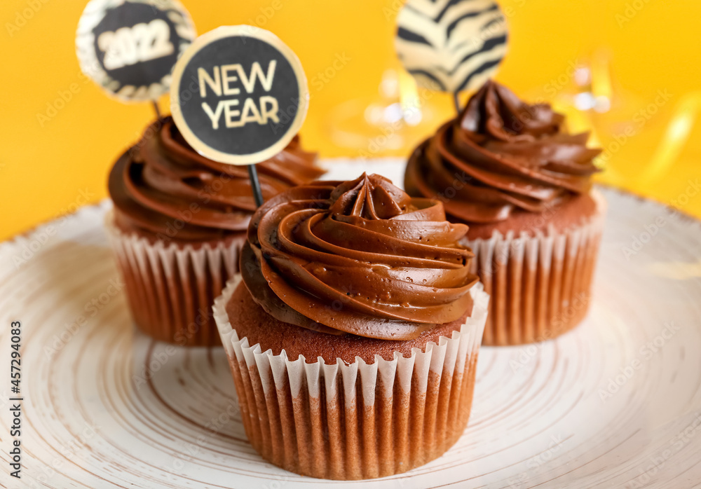 Plate with tasty cupcakes for New Year 2022 celebration on color background, closeup Plate with tasty cupcakes for New Year 2022 celebration on color background, closeup