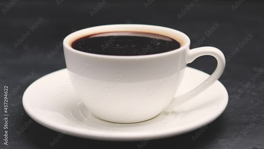 Stirring fresh brewed hot coffee in a white cup on dark background Stirring fresh brewed hot coffee in a white cup on dark background