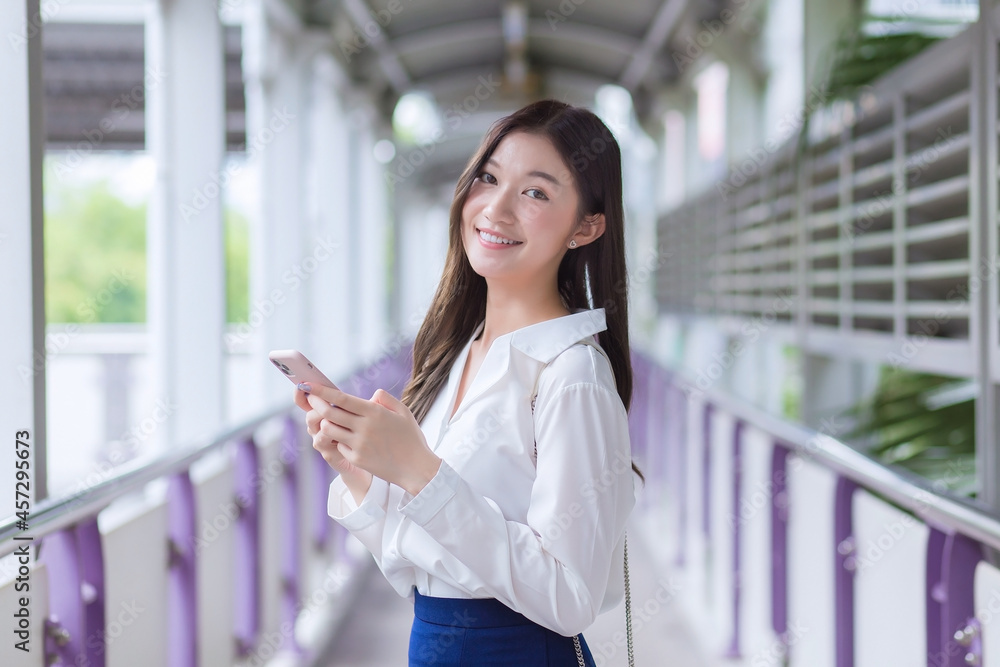Asian business beautiful woman stands on flyover of skytrain in town while uses her smartphone to send messages to someone. Asian business beautiful woman stands on flyover of skytrain in town while uses her smartphone to send messages to someone.