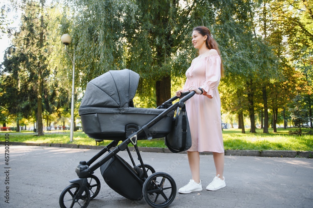 family, child and parenthood concept - happy mother walking with baby stroller in park. family, child and parenthood concept - happy mother walking with baby stroller in park.