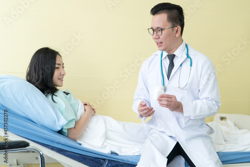 smiling man doctor holding pill bottle and consulting woman lying bed in hospital.