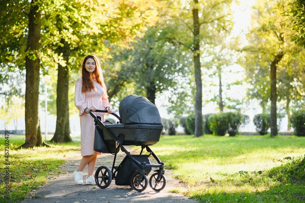 Happy young mother with baby in buggy walking in autumn park Happy young mother with baby in buggy walking in autumn park